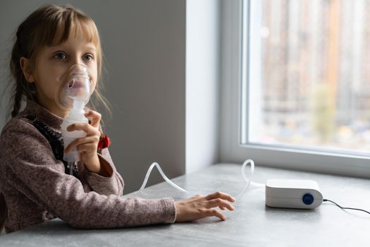 Little girl makes inhalation with a nebulizer at home, sitting on a chair. Portable apparatus for obstruction, bronchial asthma.