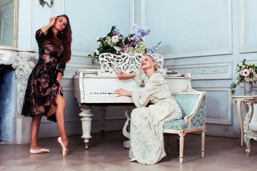 young pretty brunette ballet dancer at piano with blond woman in luxury royal interior, lifestyle rich people concept closeup