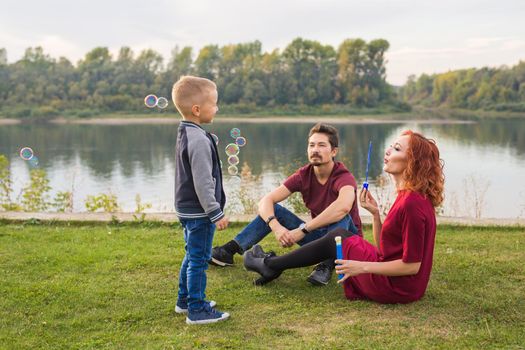 People and nature concept - Mother, father and their child playing with colorful soap bubbles.