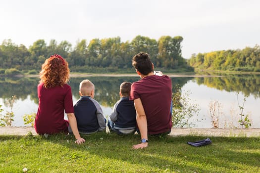 Parenthood, nature, people concept - family with two sons sitting near the lake.