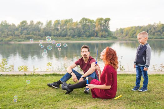 People and nature concept - Mother, father and their child playing with colorful soap bubbles.