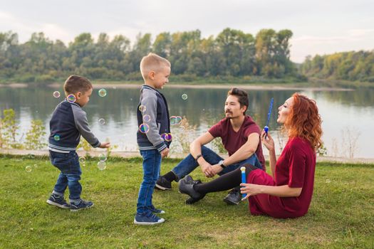 People and nature concept - Mother, father and their child playing with colorful soap bubbles.