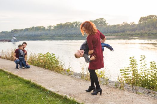 Family and children concept - mother, father and two sons enjoying the summer time, playing near the river.