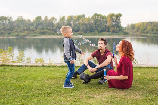 People and nature concept - Mother, father and their child playing with colorful soap bubbles.