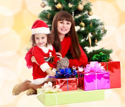 Happy mother and daughter near a Christmas tree surrounded by heaps of gifts.Winter brown abstract background with white snowflakes.