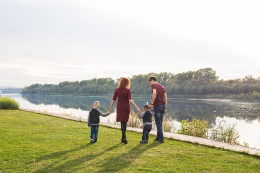 Parenthood and nature concept -Family of mother and father with two boys twins kids in a park at summer by a river at sunny day.