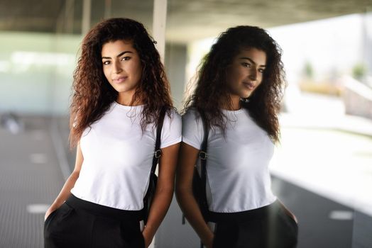 Young African woman with black curly hairstyle standing near business building. Happy Arab girl in sport clothes in the street.