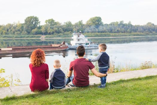 Parenthood, childhood and nature concept - Family sitting on the green ground and looking at small boat.