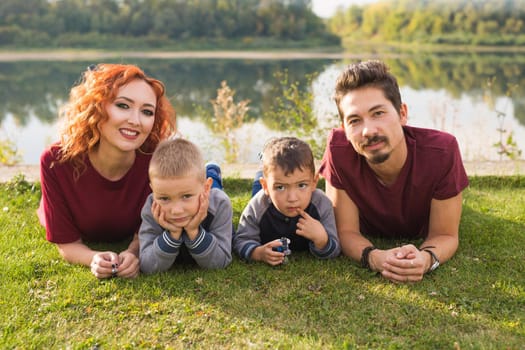 Parenthood, nature, people concept - family with two sons sitting near the lake.