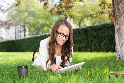 Happy young woman with digital tablet laying on grass