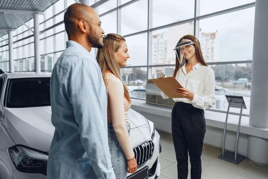 Woman car dealer consulting buyers wearing medical face shield. Coronavirus job requirements concept