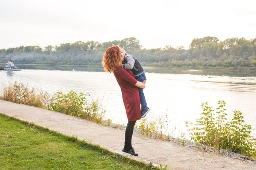 Motherhood and children concept - young mother with son in her arms near the river.