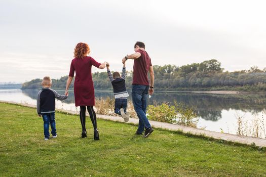 Parenthood and nature concept -Family of mother and father with two boys twins kids in a park at summer by a river at sunny day.