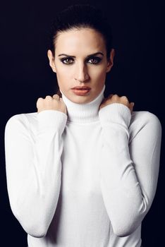 Young brunette woman wearing white poloneck. Attractive girl, model of fashion. Studio shot on black background.