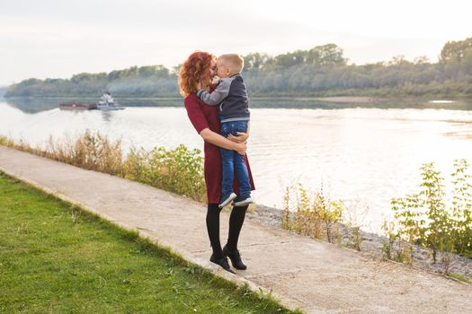 Motherhood and children concept - young mother with son in her arms near the river.