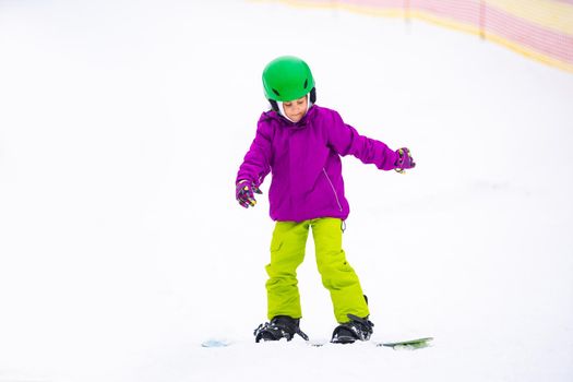 Snowboard Winter Sport. little girl learning to snowboard, wearing warm winter clothes. Winter background.