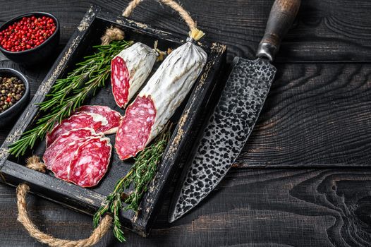 Slices of dry cured salchichon salami in a wooden tray. Black wooden background. Top view. Copy space.