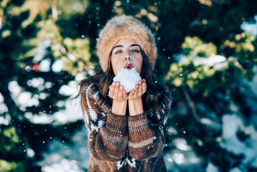 Young woman enjoying the snowy mountains in winter, in Sierra Nevada, Granada, Spain. Female wearing winter clothes playing with snow.