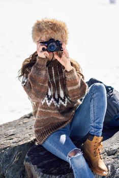 Young woman taking photographs in the snowy mountains in winter, in Sierra Nevada, Granada, Spain. Female wearing winter clothes.