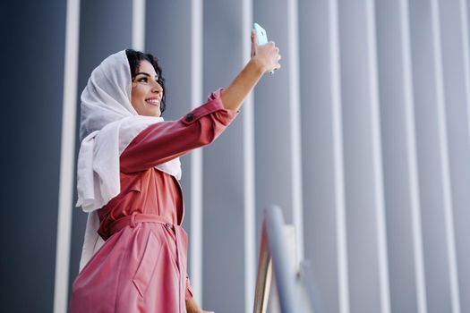Young Muslim Woman wearing hijab headscarf photograph with a smartphone in urban background