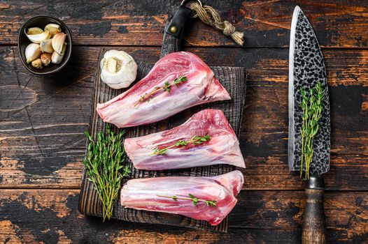 Raw lamb shanks meat on a cutting board with herbs. Dark wooden background. Top view.