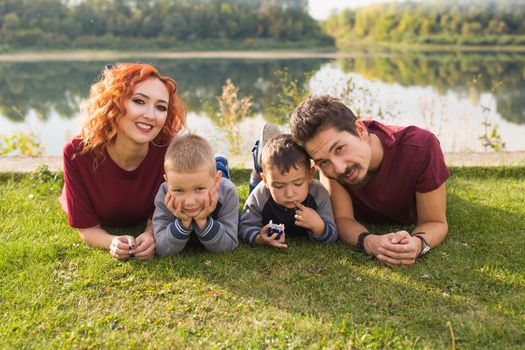 Parenthood, nature, people concept - family with two sons sitting near the lake.