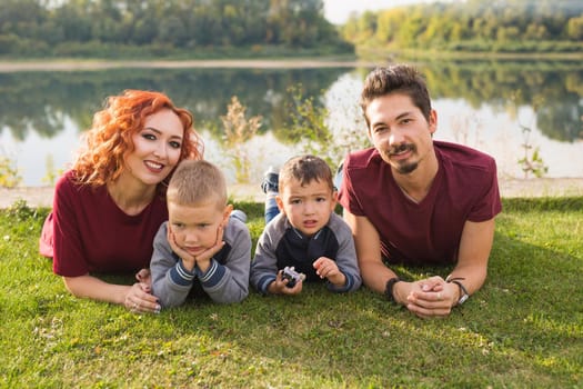 Parenthood, nature, people concept - family with two sons sitting near the lake.