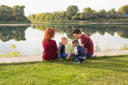 Parenthood, nature, people concept - family with two sons sitting near the lake.