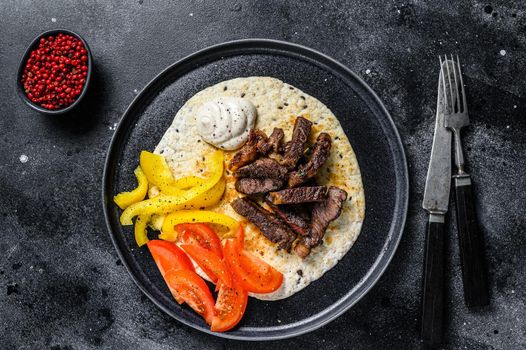 Tortilla with beef meat steak and fresh salad on a rustic plate. Black background. Top view.