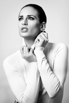 Young brunette woman wearing white poloneck. Attractive girl, model of fashion in black and white. Studio shot on white background.