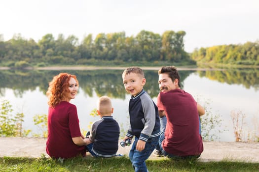 Parenthood, nature, people concept - family with two sons sitting near the lake.