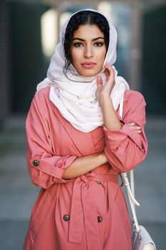 Young Muslim woman wearing hijab headscarf walking in the city center. Arab female in urban background