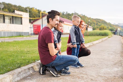 Parenthood, childhood and family concept - Parents and two male children walking at the park and looking on something.