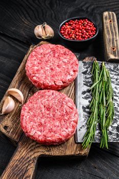 Raw steak cutlets with mince beef meat and rosemary on a wooden cutting board with meat cleaver. Black Wooden background. Top view.