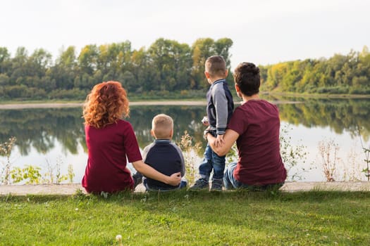 Parenthood, nature, people concept - family with two sons sitting near the lake.