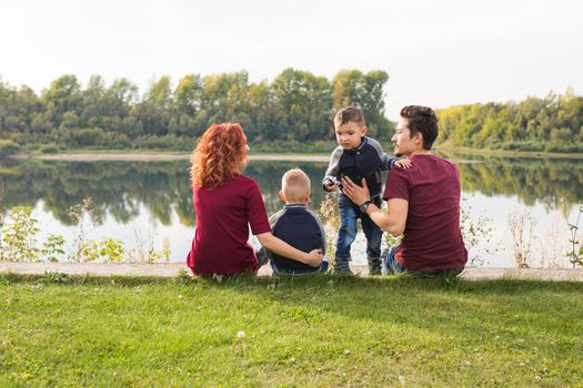 Childhood and nature concept - Family with little sons sitting on the green grass.