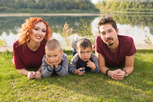 Parenthood, nature, people concept - family with two sons sitting near the lake.