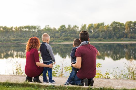 Parenthood, childhood and family concept - Parents and two male children walking at the park and looking on something.