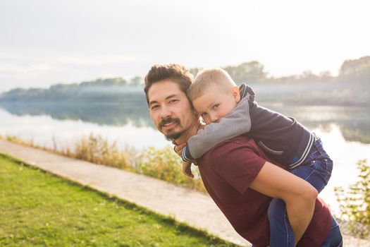 Family, childhood, fatherhood concept - Father piggyback his little son outside.