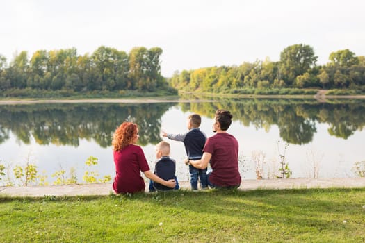 Parenthood, nature, people concept - family with two sons sitting near the lake.