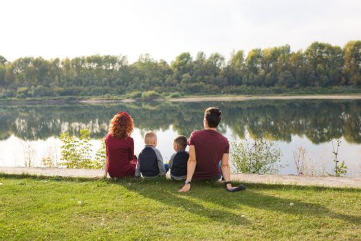 Childhood and nature concept - Family with little sons sitting on the green grass.