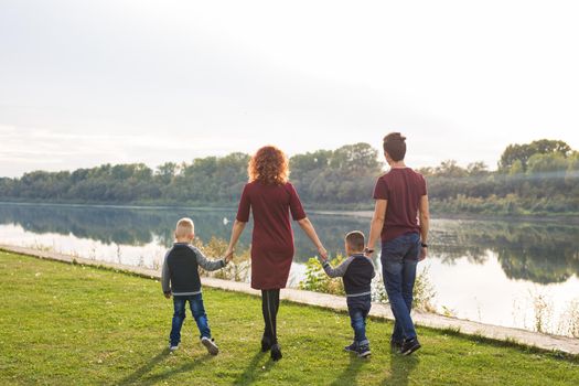 Parenthood and nature concept -Family of mother and father with two boys twins kids in a park at summer by a river at sunny day.