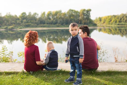 Parenthood, nature, people concept - family with two sons sitting near the lake.