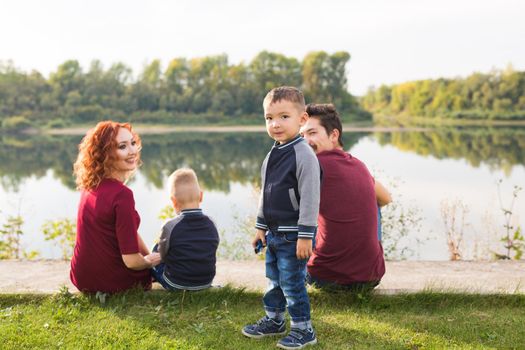 Childhood and nature concept - Family with little sons sitting on the green grass.