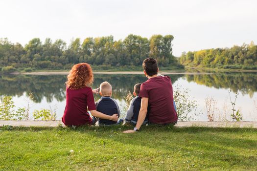 Parenthood, nature, people concept - family with two sons sitting near the lake.