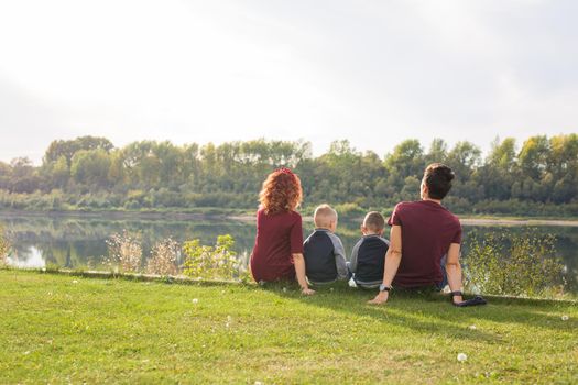 Childhood and nature concept - Family with little sons sitting on the green grass.