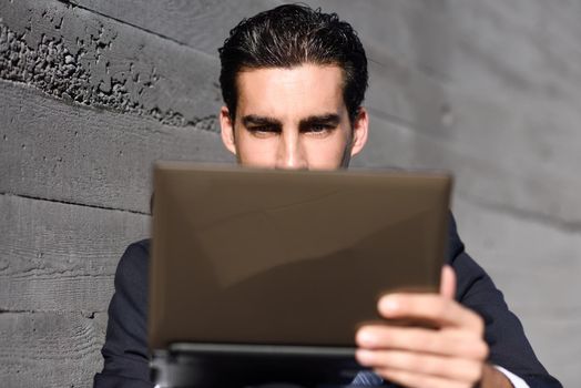 Good looking businessman using a laptop computer sitting in the street. Man wearing blue suit and tie in urban background.