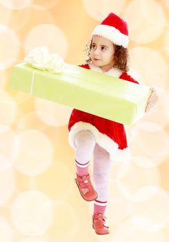 Cute little curly girl in a coat and hat of Santa Claus carries the big green box. A girl holds a box with his knee.Winter brown abstract background with white snowflakes.