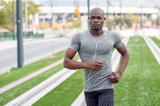 Black man running and listening to music in urban background. Handsome male doing workout outdoors.