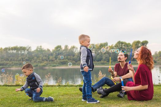 People and nature concept - Mother, father and their child playing with colorful soap bubbles.